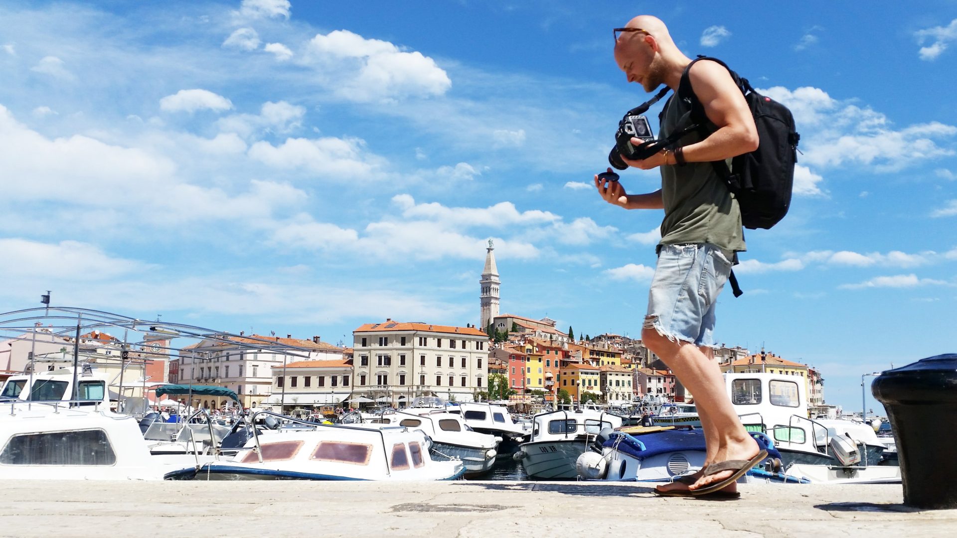 man walking along a pier in croatia with a camera and blue sky