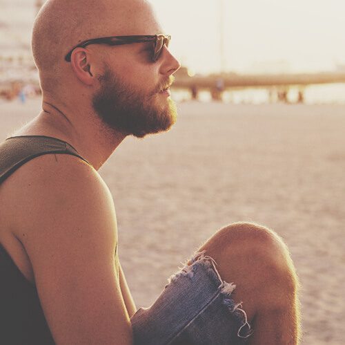 man looking at the sunset from the beach with sunglasses