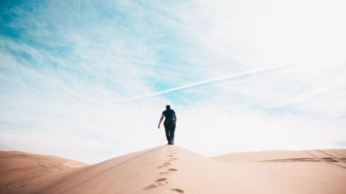 Man walking up sand dune in the desert